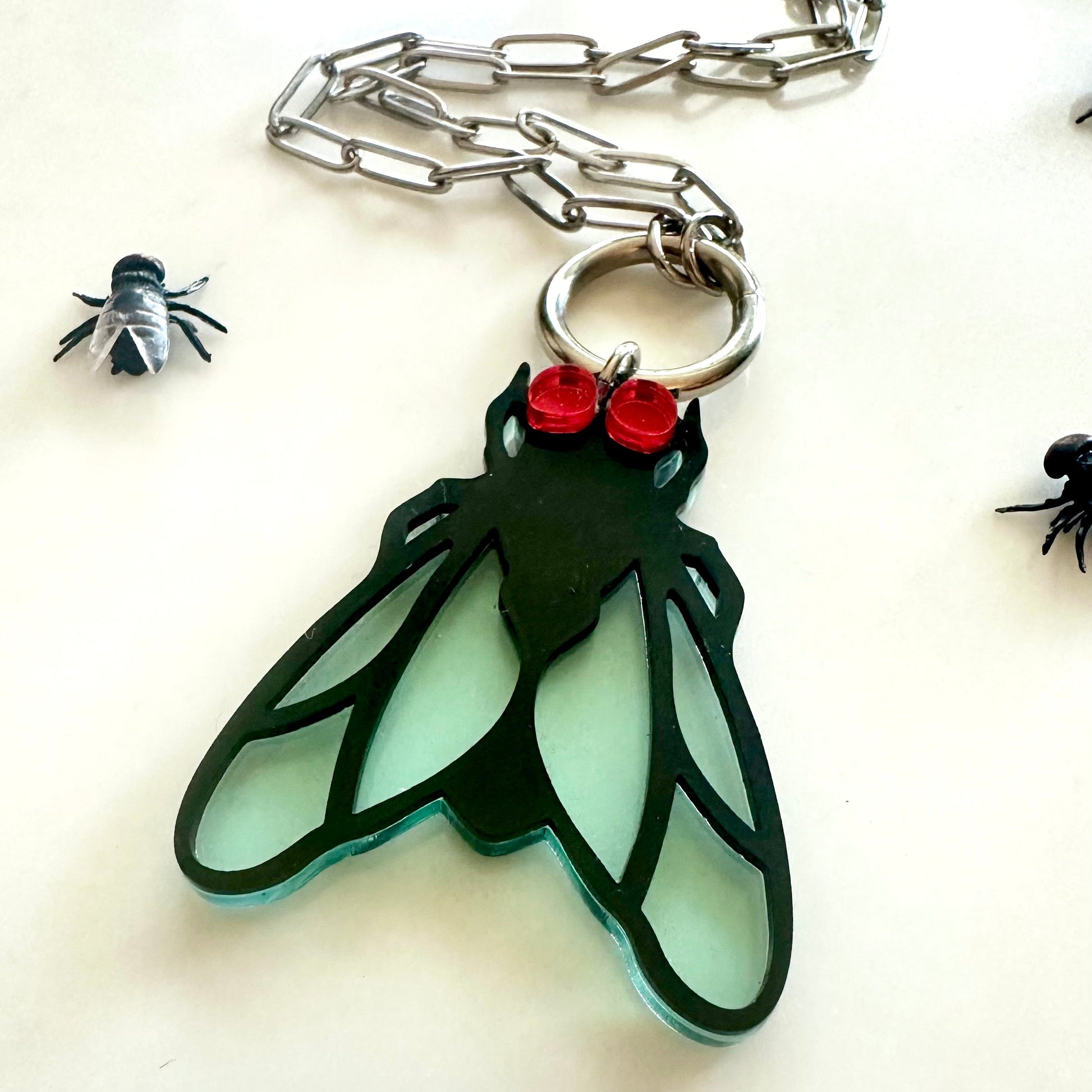 Insect-shaped pendant with red accents on a chain against a white background