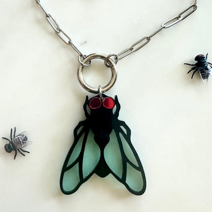 Pendant shaped like a fly with red eyes on a chain, surrounded by small black flies on a white background