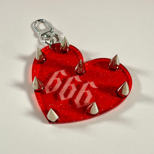 Red heart-shaped keychain with silver spikes and the number 666 on a light gray background