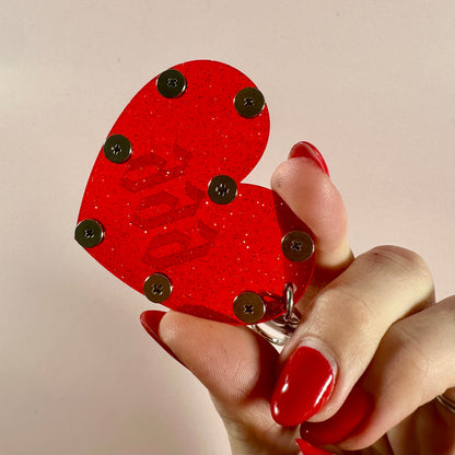Red heart-shaped keychain with 'love' text held by a hand with red nails against a beige background