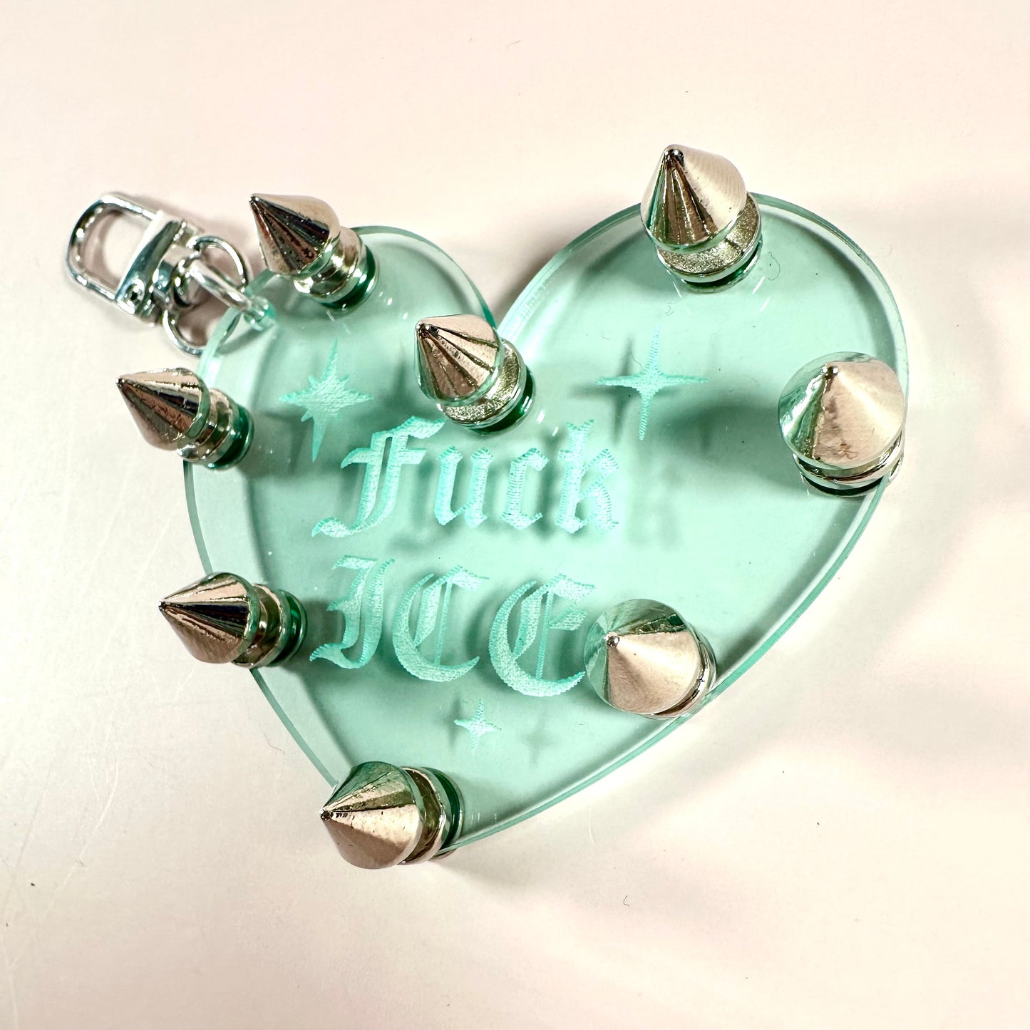 Heart-shaped object with spikes and 'F**k Love' engraving on a light background