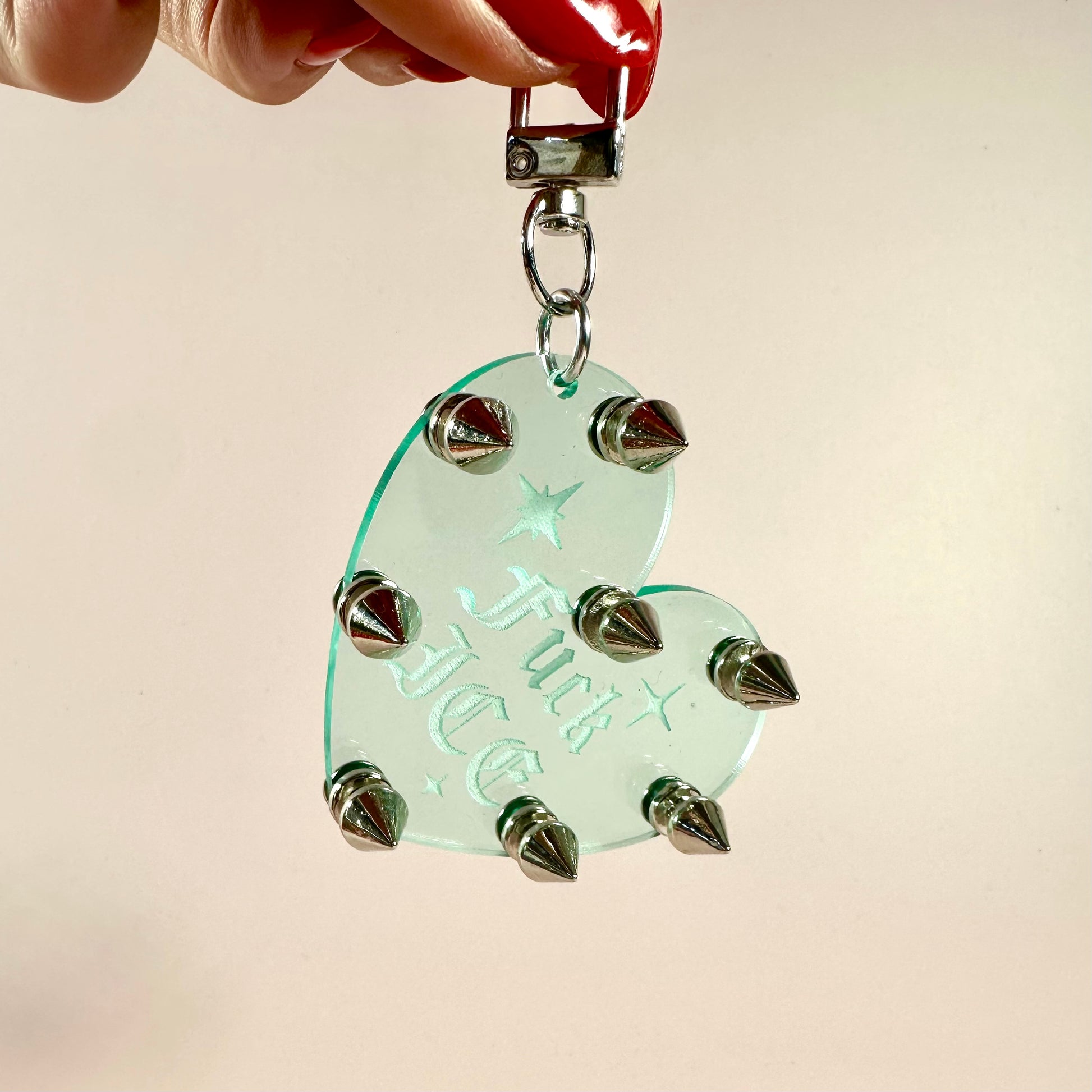 Heart-shaped pendant with spikes held by a hand against a beige background