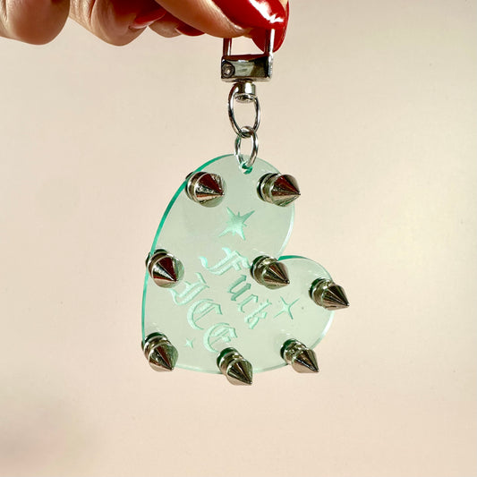 Heart-shaped pendant with spikes held by a hand against a beige background