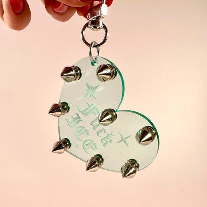 Heart-shaped keychain with spikes held by a hand against a pink background