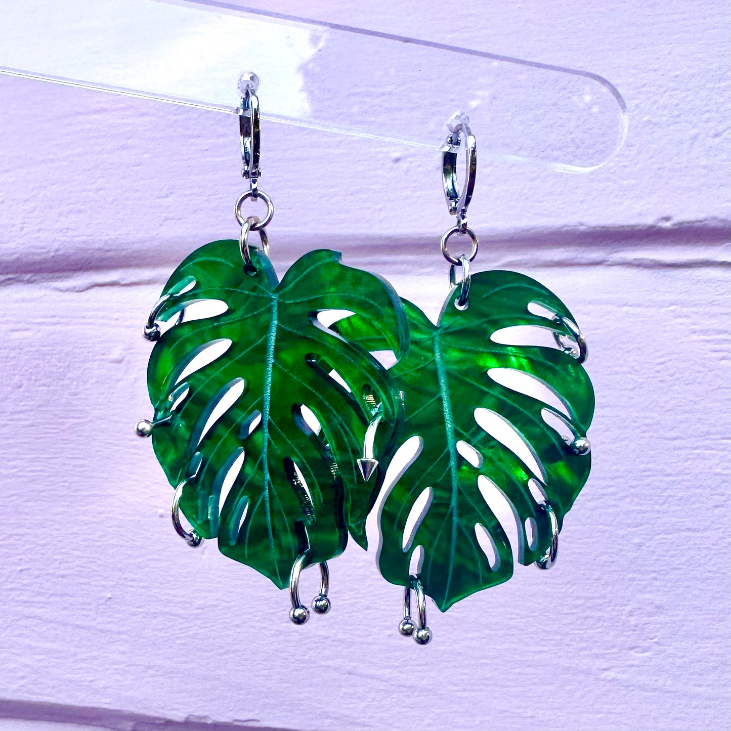Green leaf-shaped earrings on a clear stand against a white background
