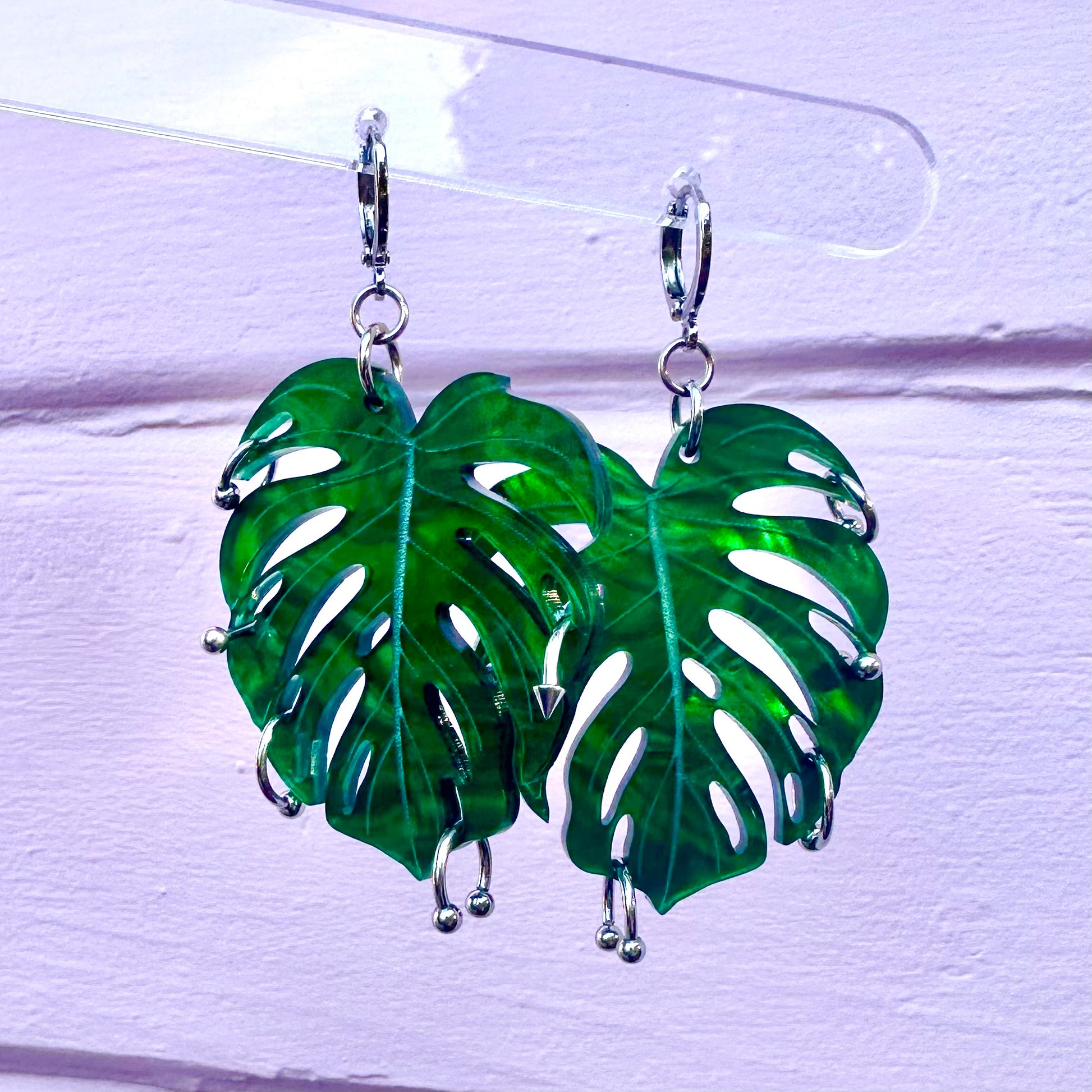 Green leaf-shaped earrings on a clear stand against a white background