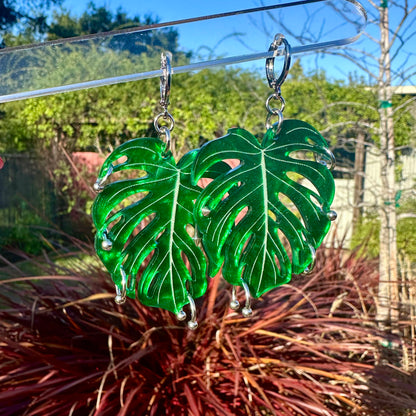 Green leaf-shaped earrings on a clear stand with a garden background