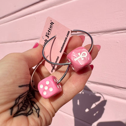 Pink dice-shaped keychains with a ring held by a hand against a pink background