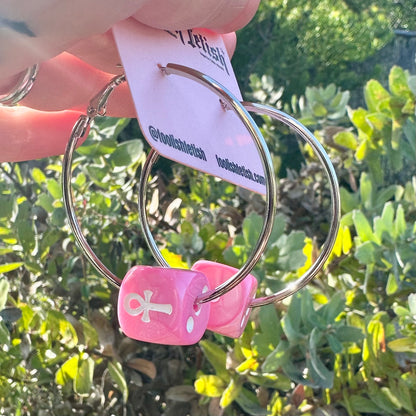 Keychain with pink dice and silver rings held by a hand against a green leafy background