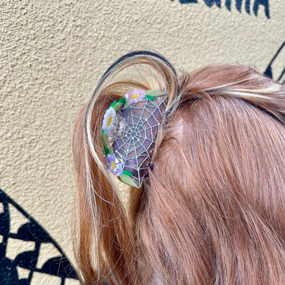 Person with decorative hair clip featuring a spiderweb design against a textured wall.