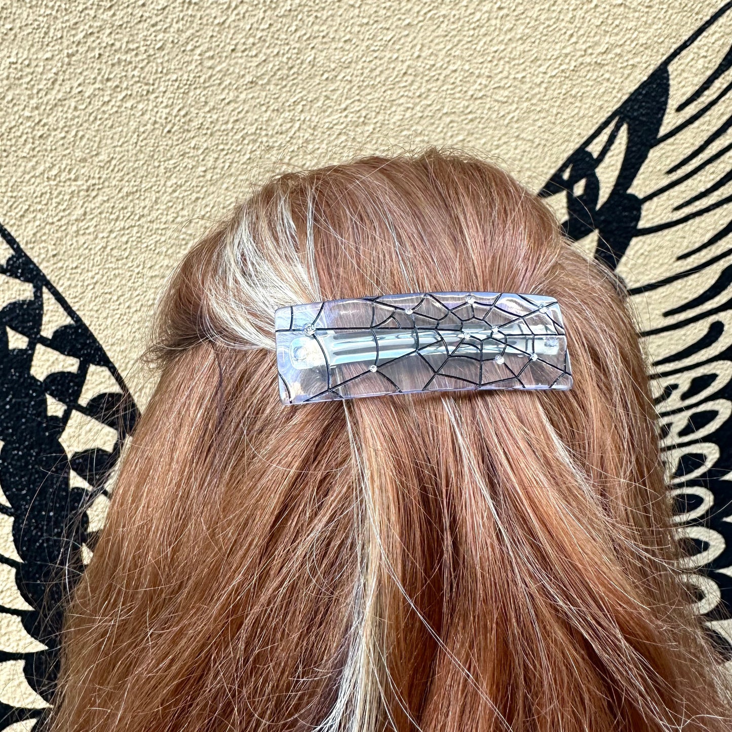 Person with a decorative hair clip in their hair against a patterned wall.