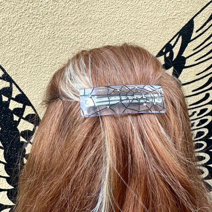 Person with a decorative hair clip in their hair against a patterned wall.