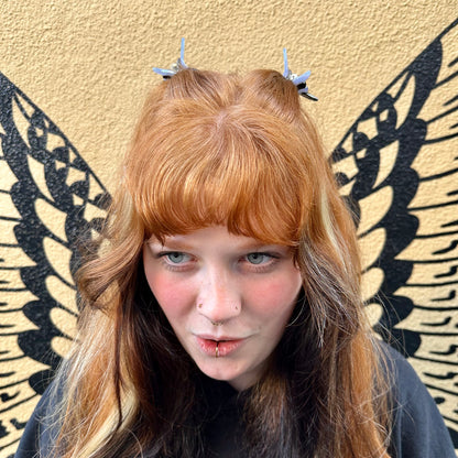 Person with red hair and blue hair clips against a beige wall with butterfly wings.