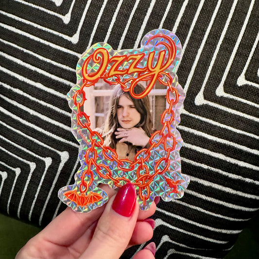 Decorative mirror with 'Ozzy' text held by a hand against a striped background