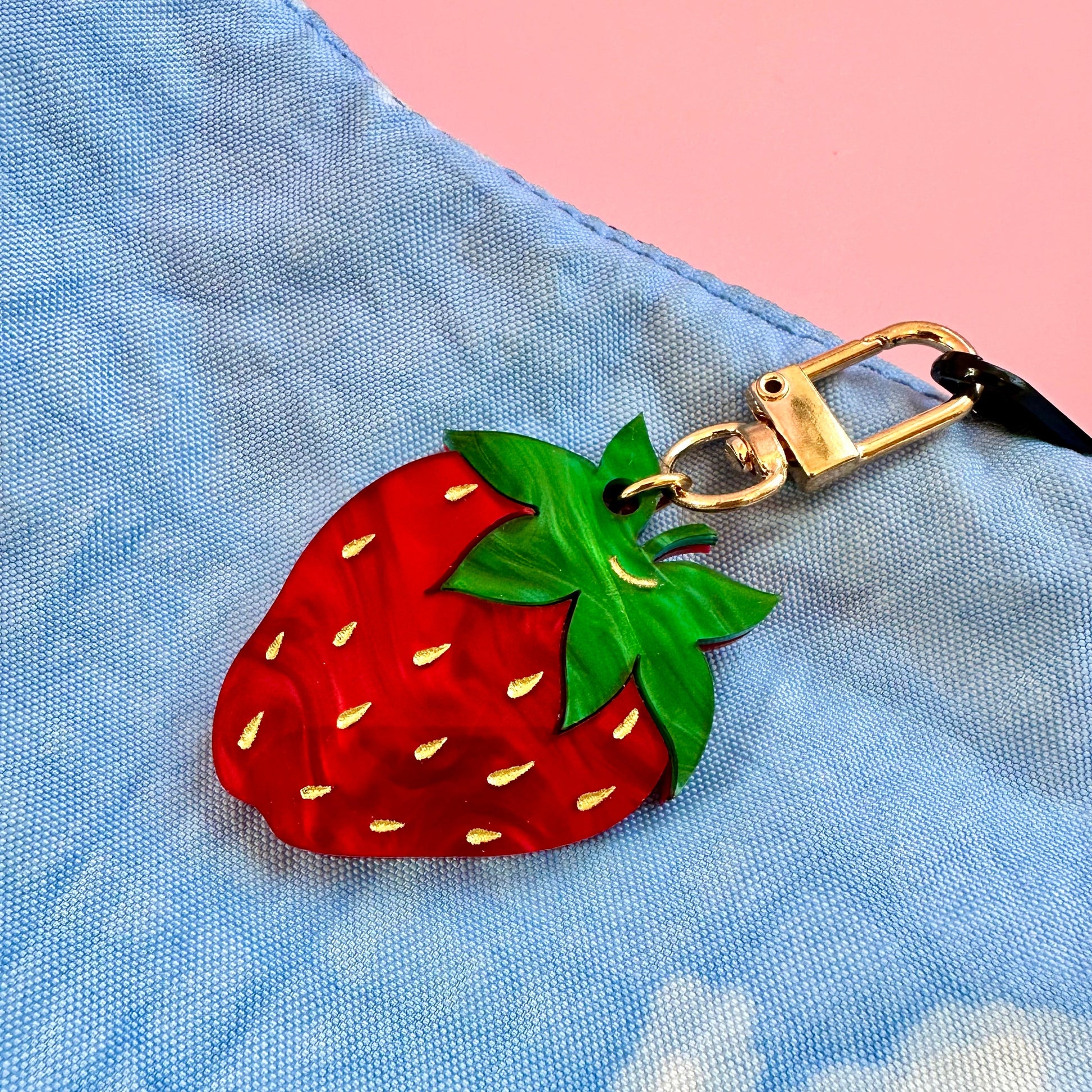 Strawberry-shaped keychain attached to a blue bag with a pink background