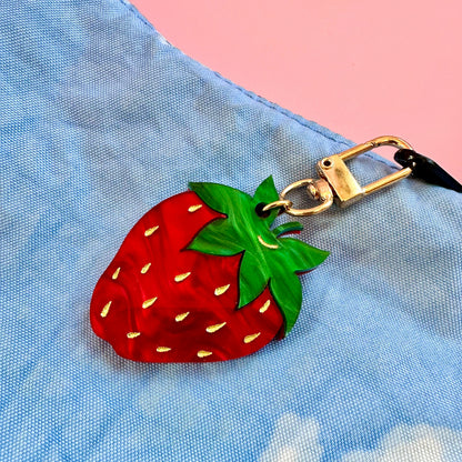 Strawberry-shaped keychain attached to a blue bag with a pink background