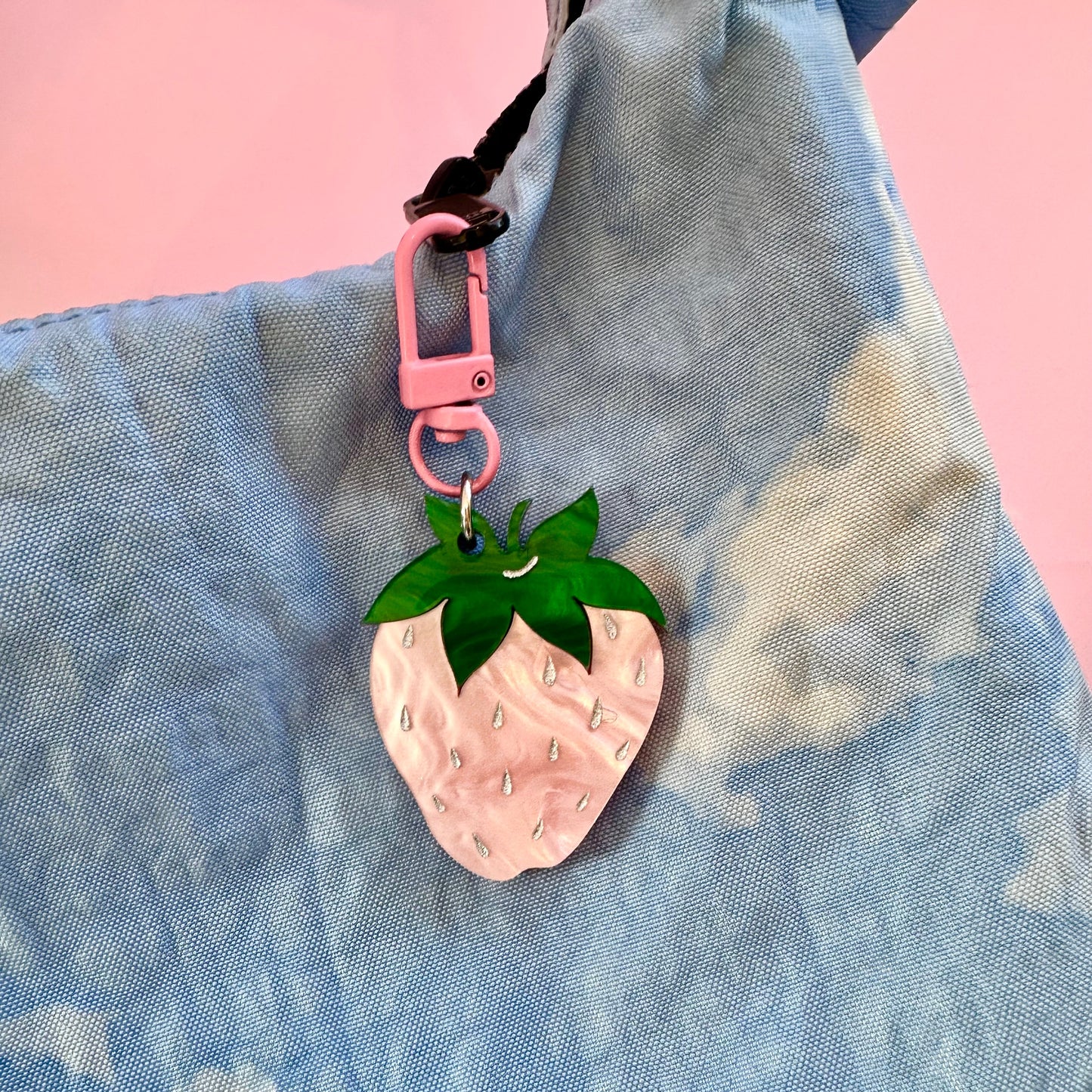 Pink strawberry-shaped keychain on a blue textured surface with a pink background