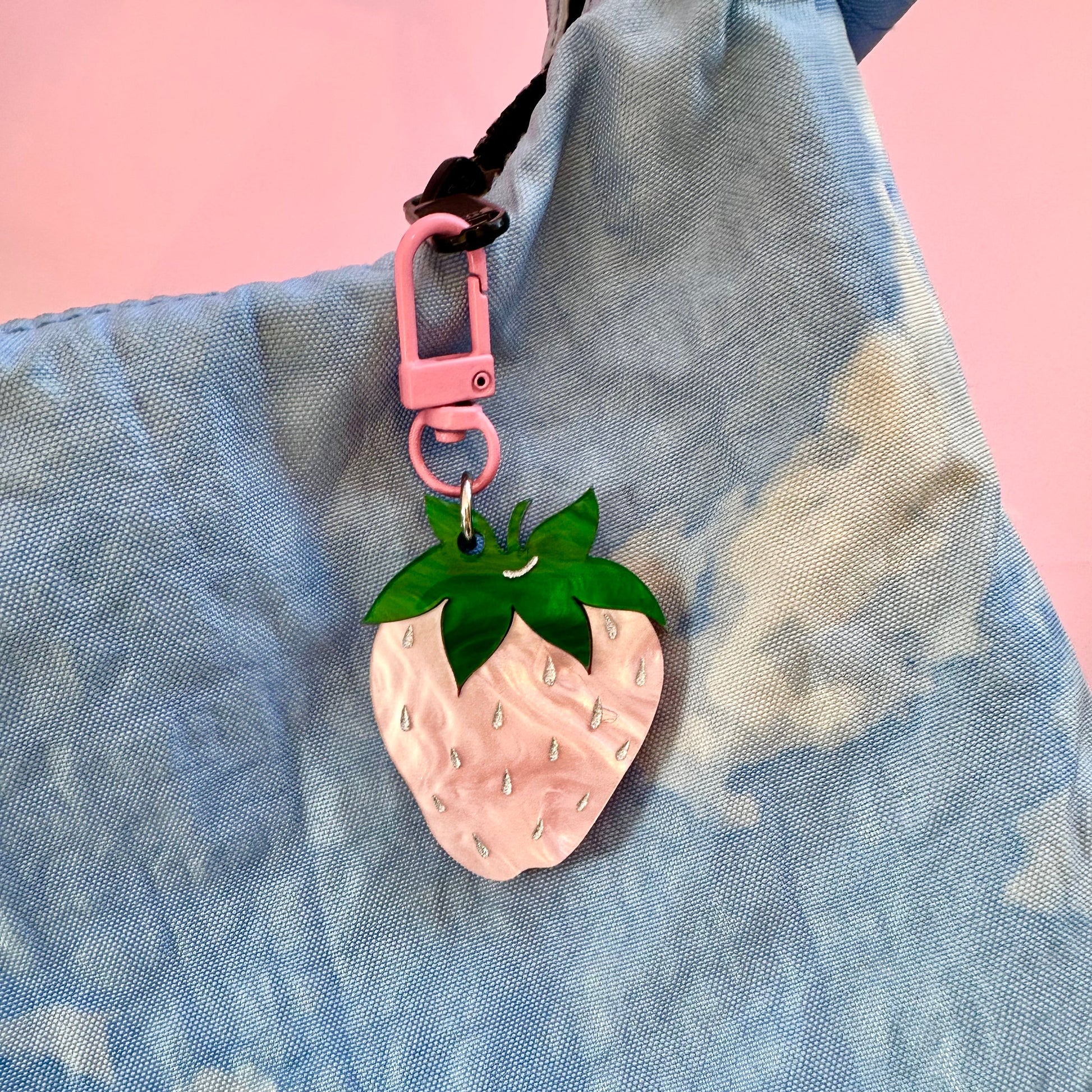 Pink strawberry-shaped keychain on a blue textured surface with a pink background