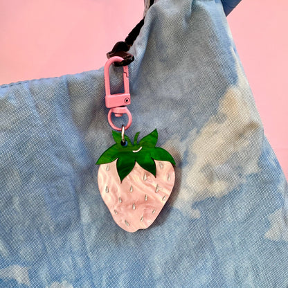 Pink strawberry-shaped keychain on a blue textured surface with a pink background