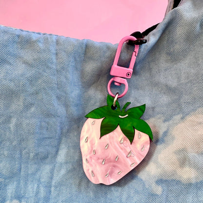 Pink strawberry-shaped keychain with green leaves on a blue textured background