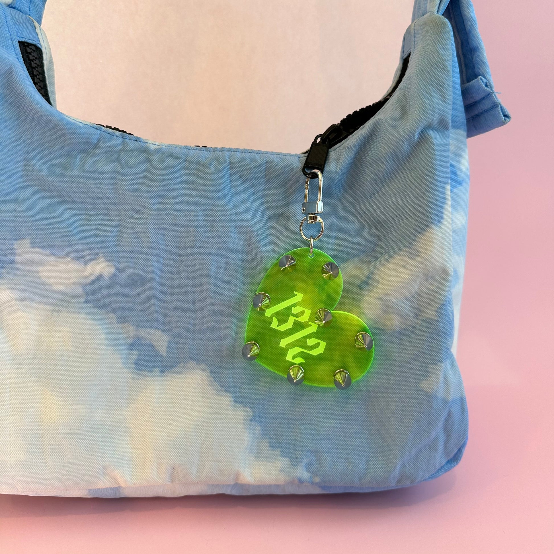 Heart-shaped green tag with '1312' on a blue tie-dye bag against a pink background