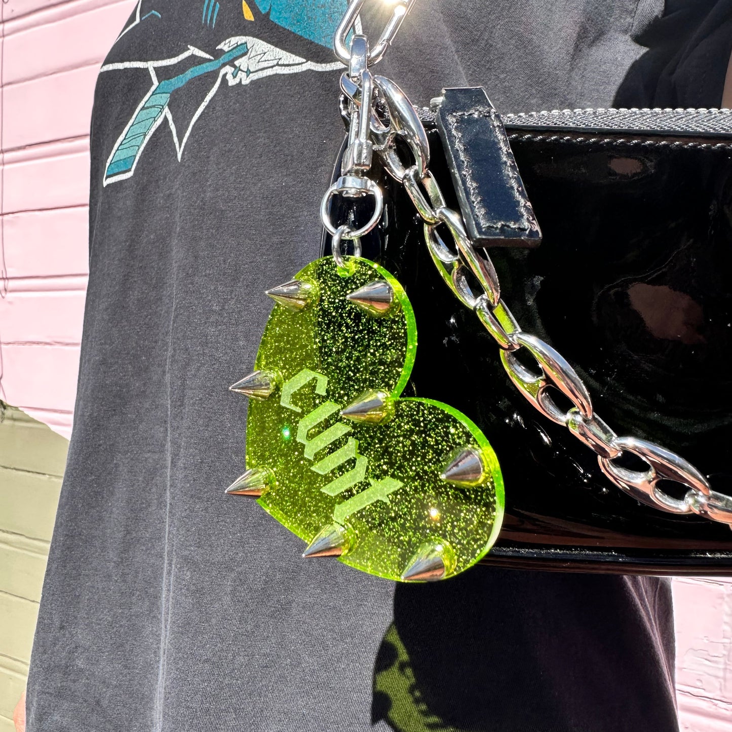 Green glittery heart-shaped charm with 'Cunt' on a black bag.