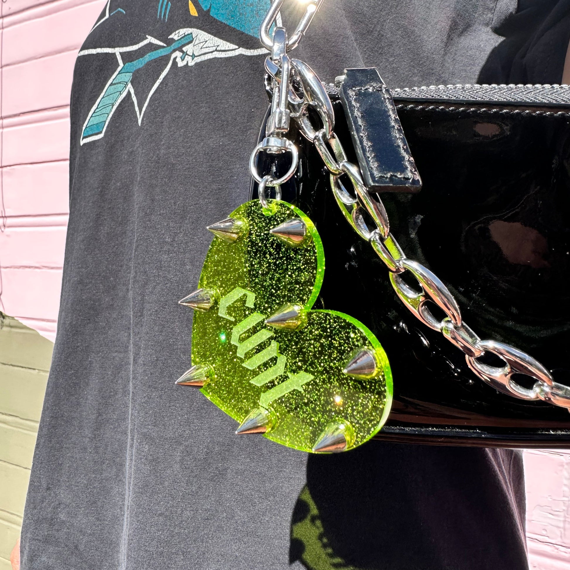 Green glittery heart-shaped charm with 'Cunt' on a black bag.