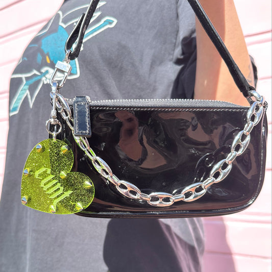 Black handbag with a chain strap and heart-shaped tag on a person wearing a gray shirt.