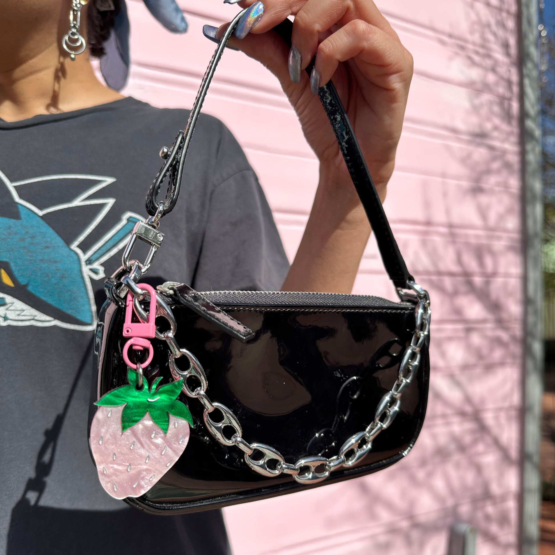 Black handbag with chain detail held by a person against a pink vehicle background