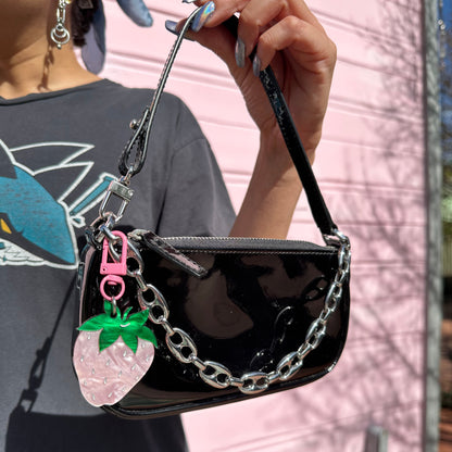 Black handbag with chain detail held by a person against a pink vehicle background