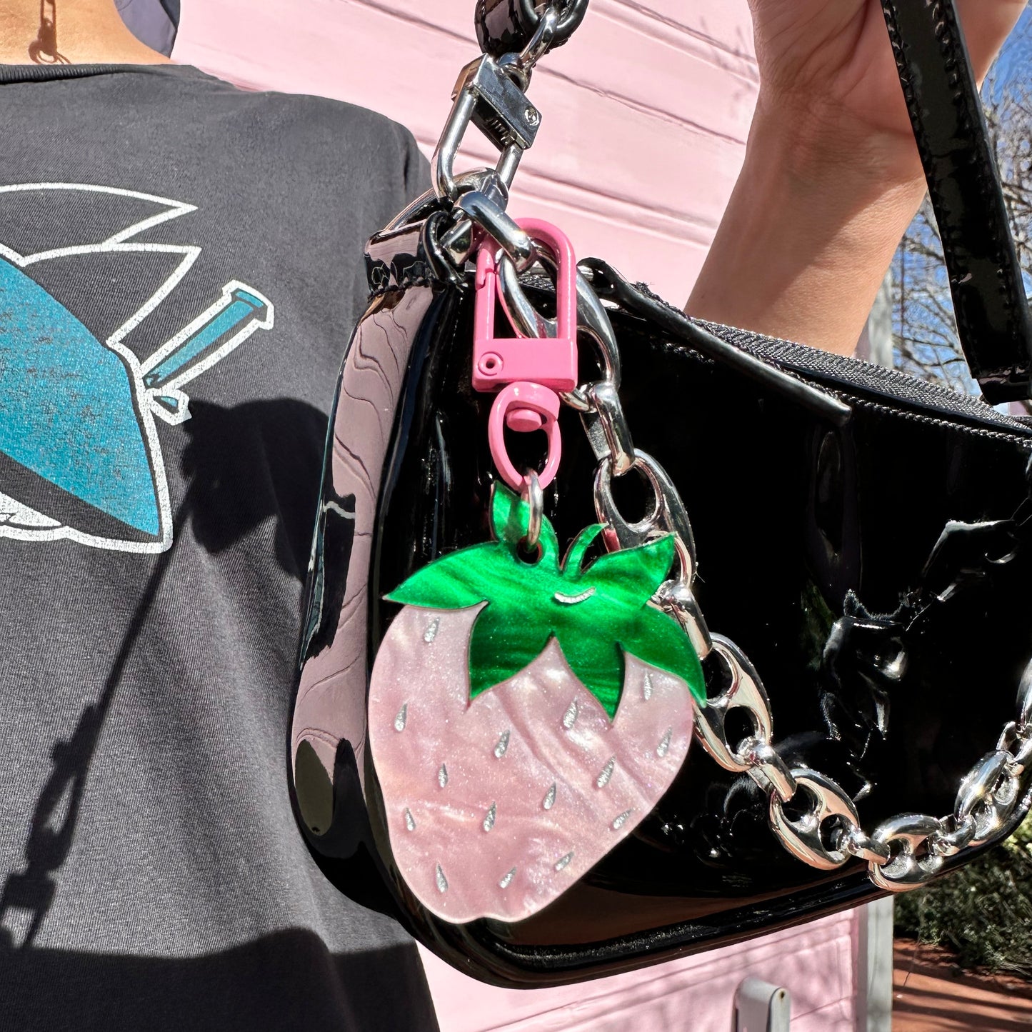 Black handbag with pink strawberry charm and green leaves on a blurred background
