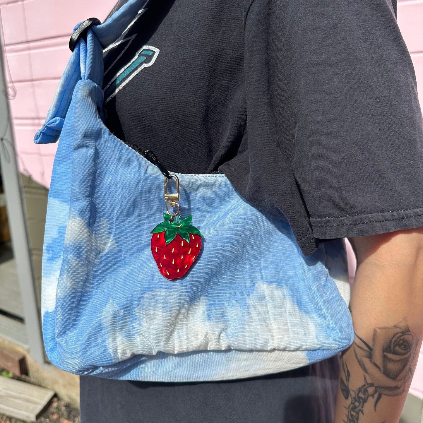 Blue bag with a strawberry design held by a person wearing black pants.