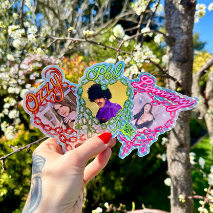 Hand holding a set of colorful stickers with images and text, against a natural background with trees and flowers.