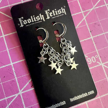 Silver chain and star earrings on a Foolish Fetish branded card against a pink grid background.
