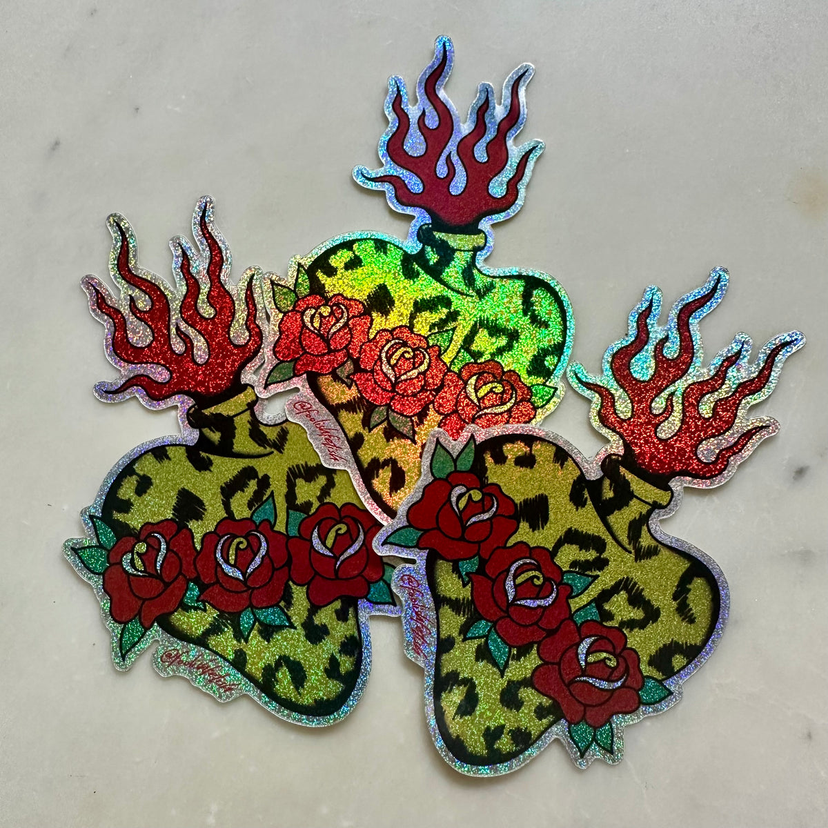 A set of three glittery, die-cut stickers featuring green leopard-print vases with red roses and red flames, displayed on a light marble surface.