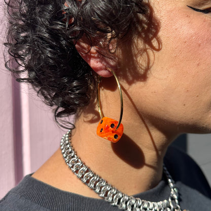 Close-up of a person wearing a silver chain necklace and an orange earring with black details.