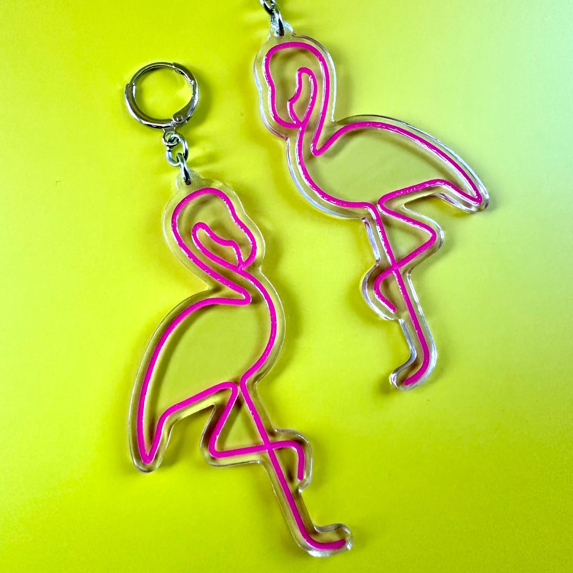 Two flamingo-shaped earrings with silver metal rings, featuring a hot pink outline on a bright yellow background.