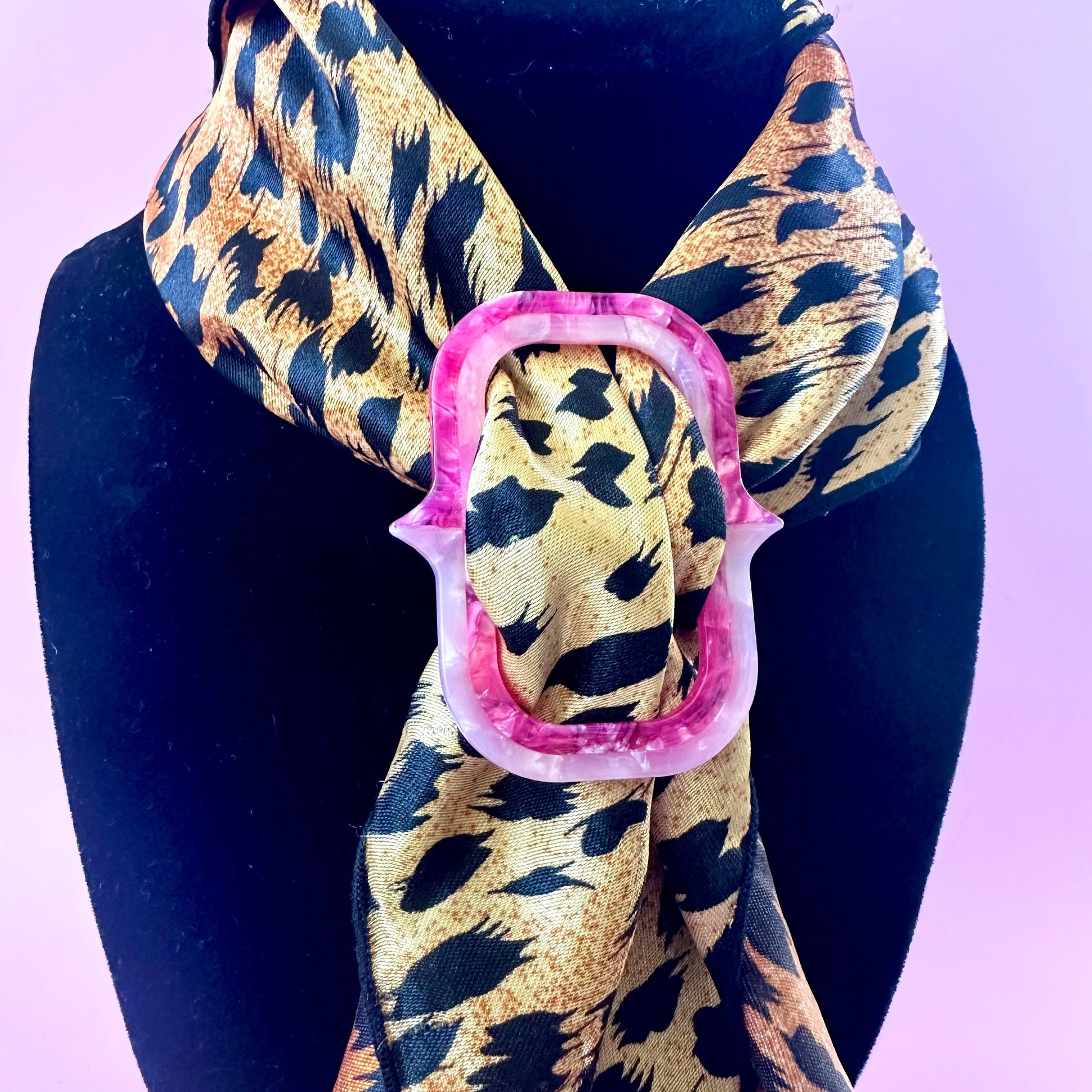 A leopard print scarf with a pink decorative ring accent, displayed on a black mannequin bust against a light purple background.
