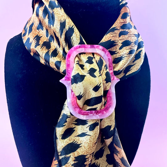 A leopard print scarf with a pink decorative ring accent, displayed on a black mannequin bust against a light purple background.