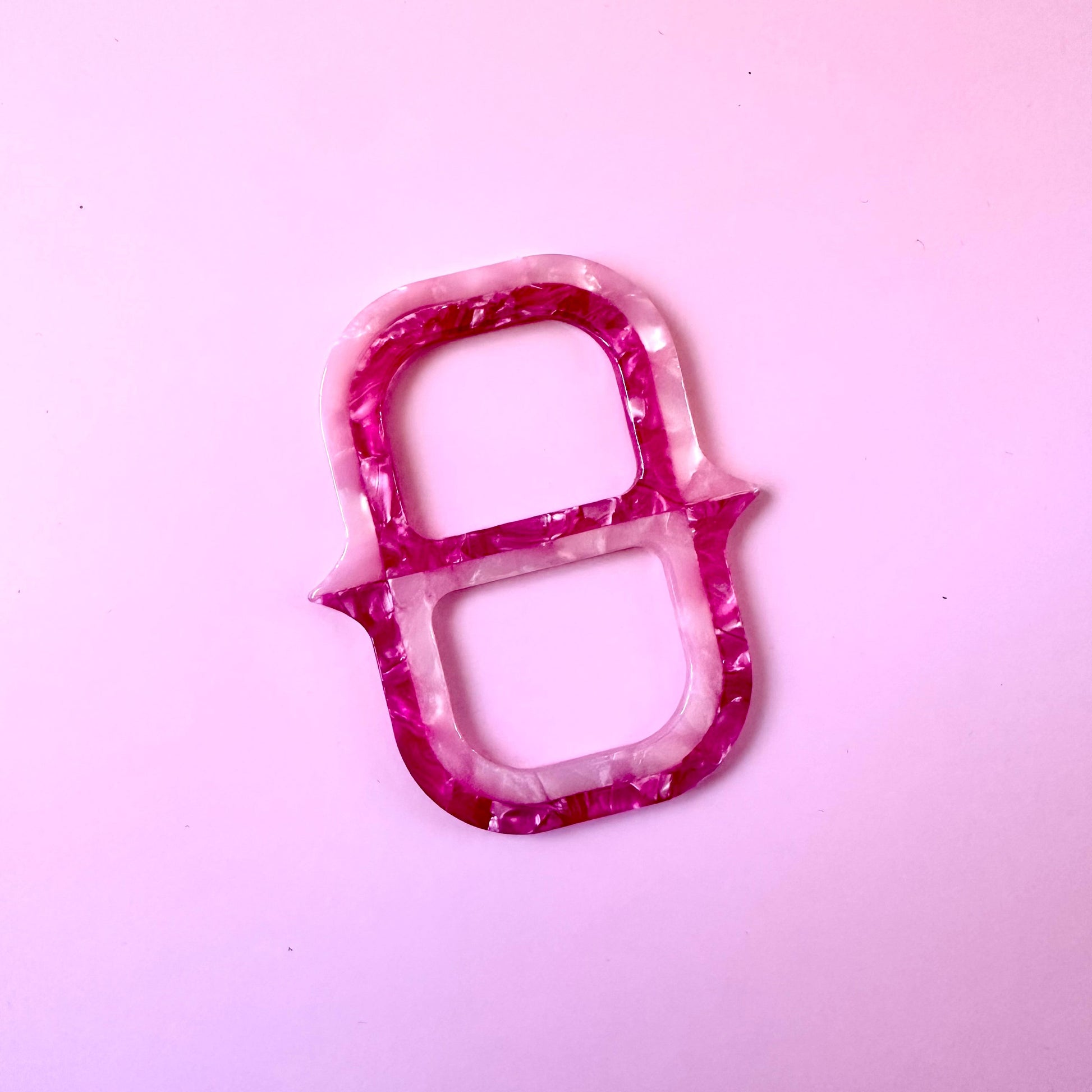 A small decorative scarf ring  with a marbled pink and white pattern, photographed on a solid light pink background.