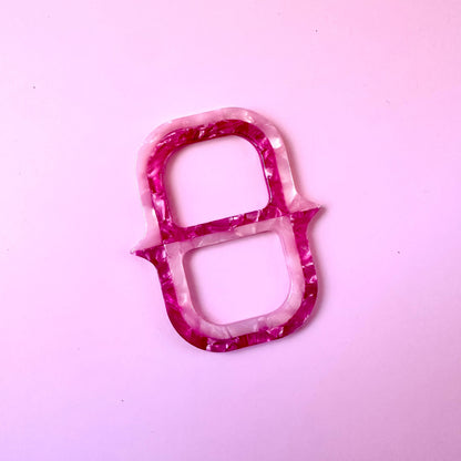 A small decorative scarf ring  with a marbled pink and white pattern, photographed on a solid light pink background.