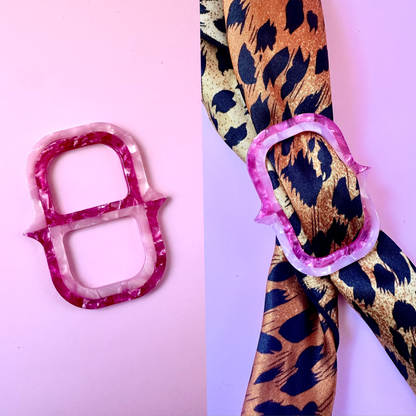 A pink and white marbled ring-shaped accessory shown on a pink background, alongside a leopard-print ribbon tied with a matching pink ring.