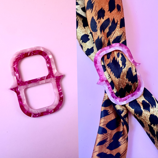 A pink and white marbled ring-shaped accessory shown on a pink background, alongside a leopard-print ribbon tied with a matching pink ring.