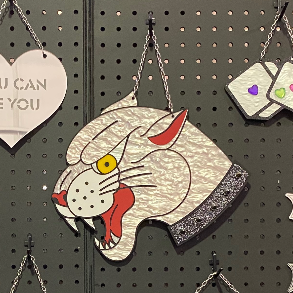 Decorative earrings hanging on a pegboard with a cat-shaped earring and butterfly earring.