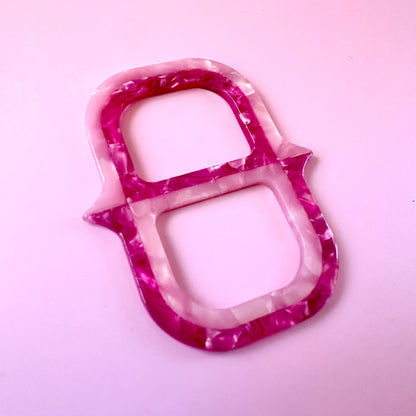 A translucent scarf ring holder with a marbled pink and white pattern, photographed on a solid light pink background.