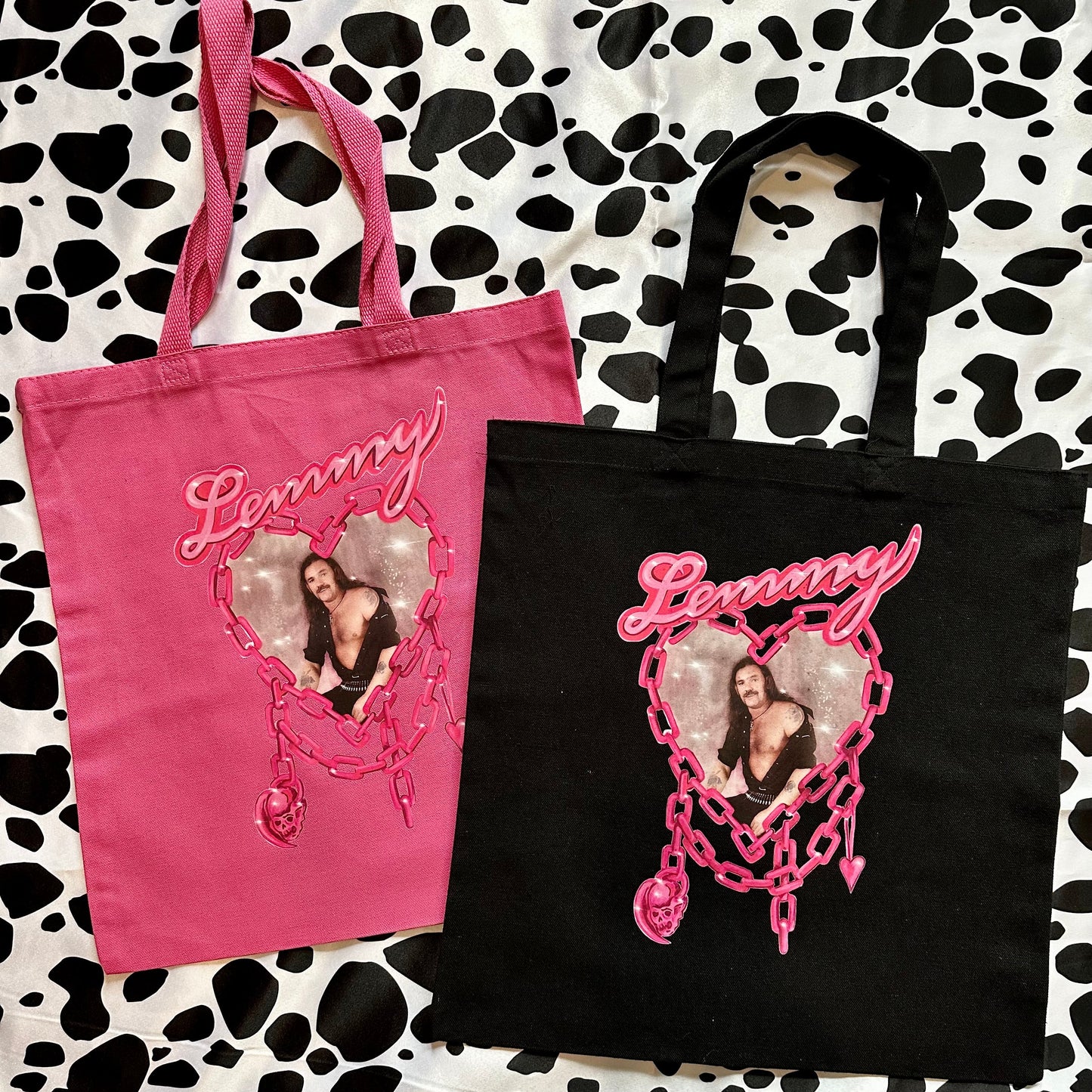 Two custom canvas tote bags, one pink and one black, displayed on a black and white cow print background. Each bag features a custom heart-shaped photo print and the name 'Lemmy' in pink script.