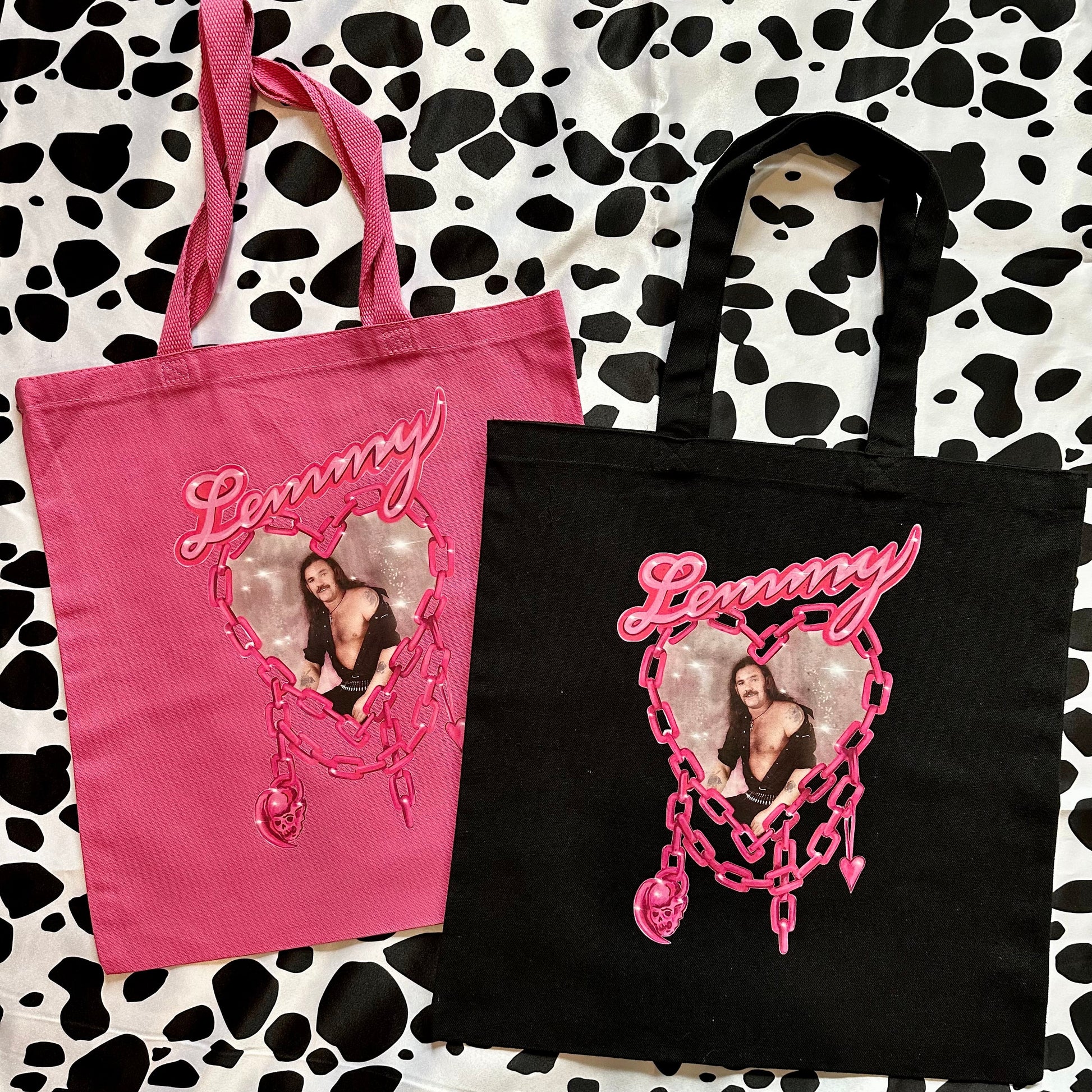 Two custom canvas tote bags, one pink and one black, displayed on a black and white cow print background. Each bag features a custom heart-shaped photo print and the name 'Lemmy' in pink script.
