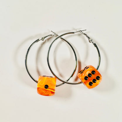 Hoop earrings with orange dice-shaped charms on a light background