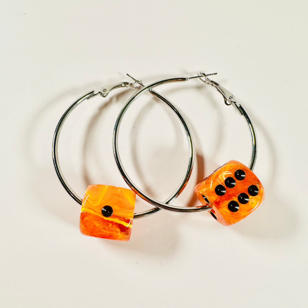 Hoop earrings with orange dice-shaped charms on a light background