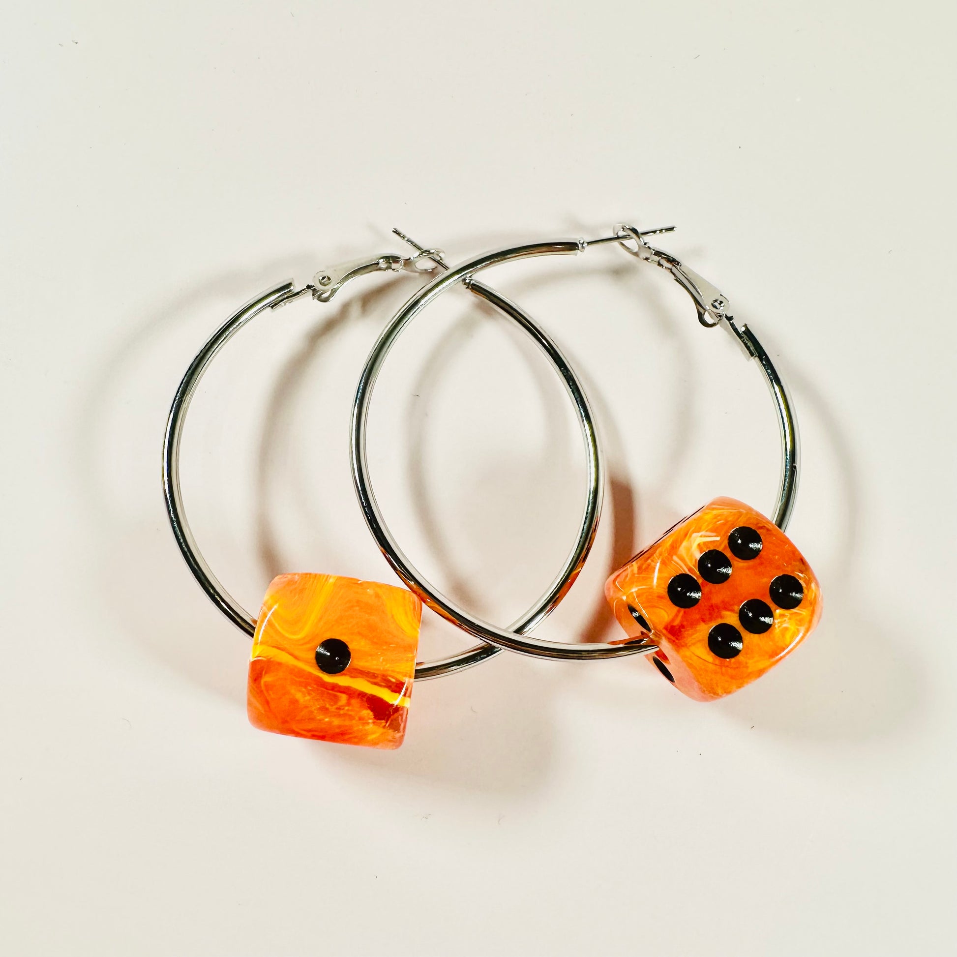 Hoop earrings with orange dice-shaped charms on a light background